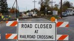 Road closed sign blocking a street at a railroad crossing with construction workers and vehicles beyond.